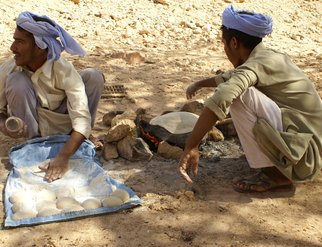 Two Bedouin men sitting on the ground, skillfully making traditional bread